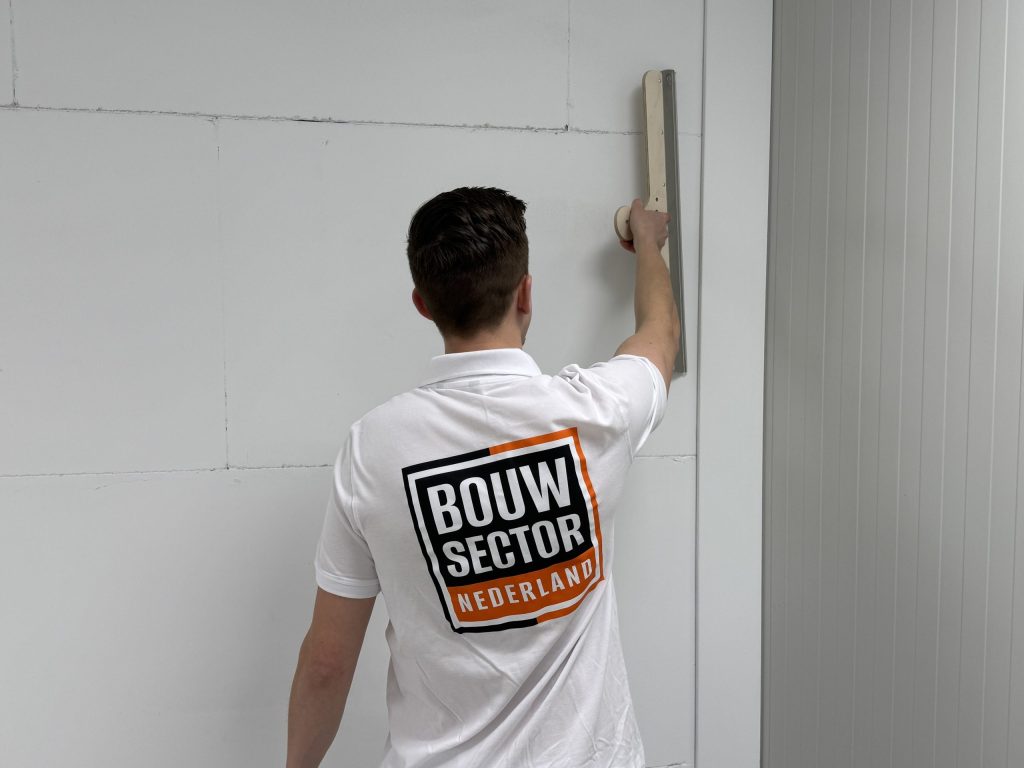 Stukadoor van Bouwsector Nederland zet een lange rei rechtop tegen de wand, van achteren gezien