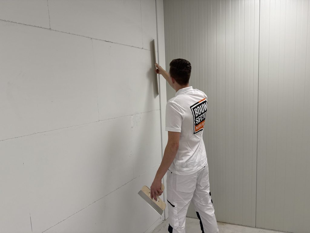Vakman van Bouwsector Nederland trekt een rei langs een lange wand naast een geribde roldeur