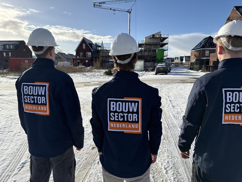 Drie medewerkers van Bouwsector Nederland met witte helm kijken naar bakstenen woningen in aanbouw